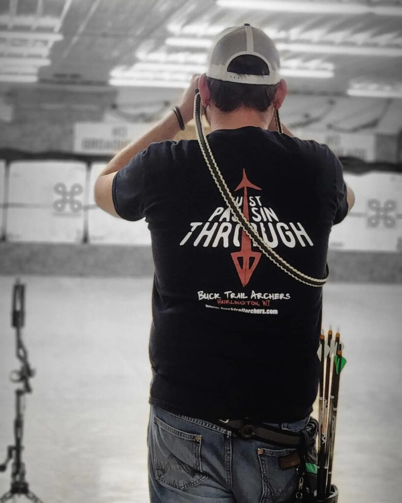 Man ready to shoot a bow and arrow and showing Buck Trail Archers t-shirt which says "Just Passin Through".