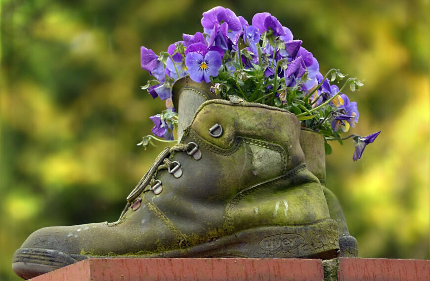 A set of work boots with purple flowers blooming from the top of the boots.