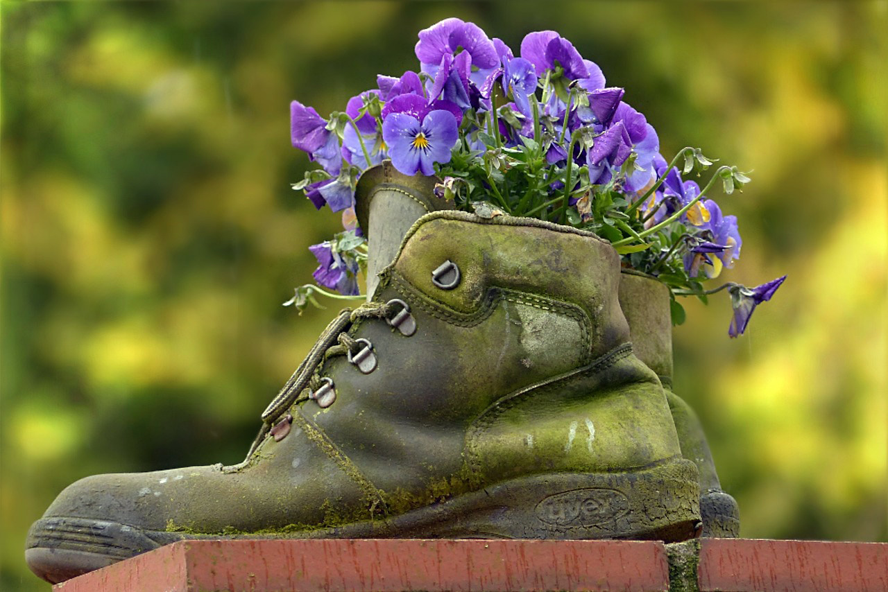 A set of work boots with purple flowers blooming from the top of the boots.