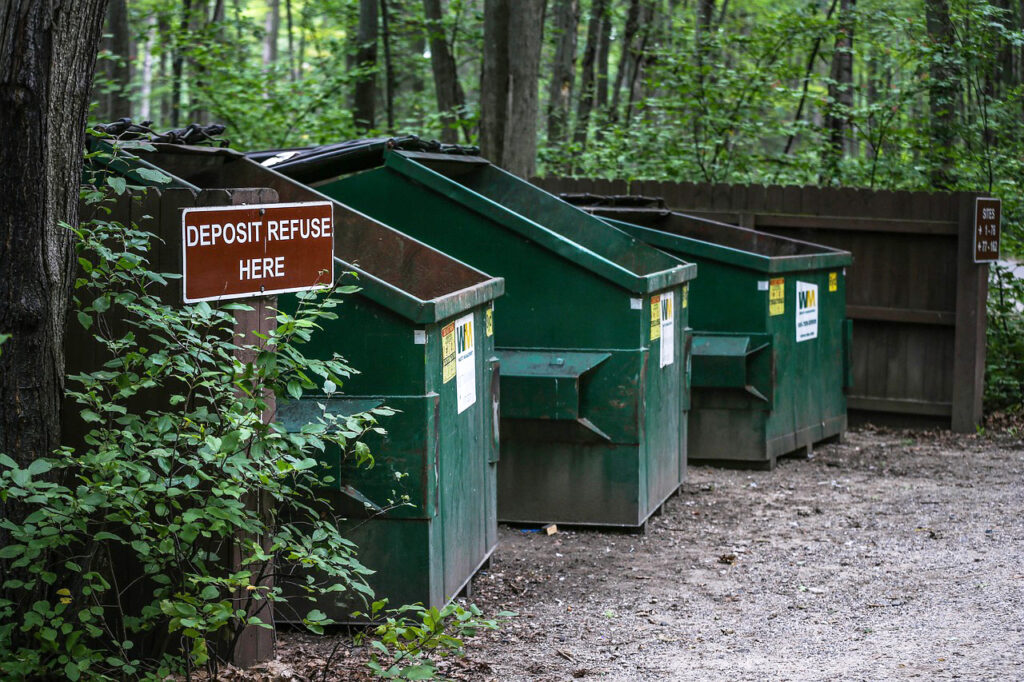 Three Commercial Garbage and Recycling Bins in the Woods.